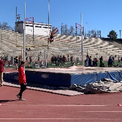 Student photographed over the high jump bar about to land on the other side.