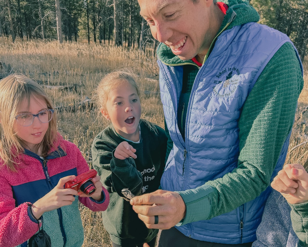 A teacher holding an insect while two students look amazed.