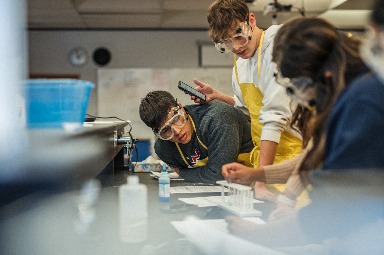 Three students wearing goggles participate in a science lab exercise.