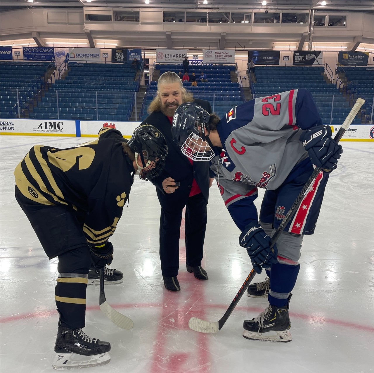 Hockey players from both Liberty and Battle Mountain high schools face off while former Coach Walt Aufderheide drops the puck.