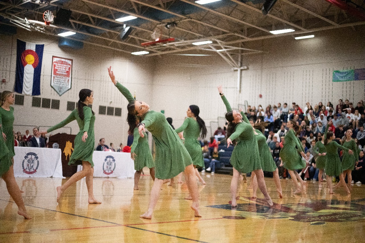 Liberty dancers perform in Liberty's gym in front of the student body in bleachers and Liberty principals sitting at a nearby table with Liberty's crest on the tablecloth.