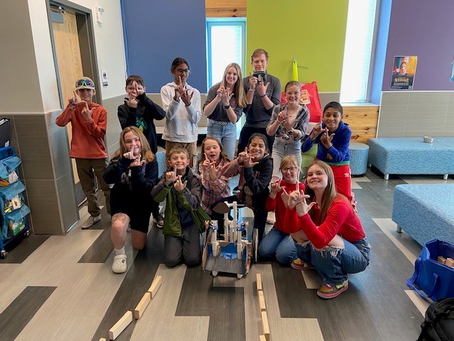 Liberty robotics students and students from Legacy Peak Elementary picture with their robot holding up double L's with their fingers.