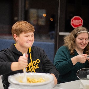 Liberty student stirs a pot of mac n' cheese while another student sit nearby.