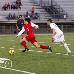Liberty soccer player runs with the ball ahead of an opponent in front of the referee on the soccer field.