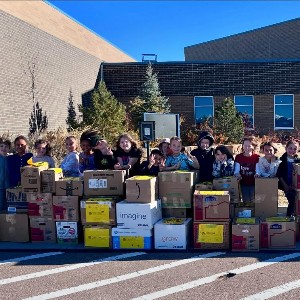 Students standing in front of a wide variety of boxes donated during the Harvest of Love donation drive.