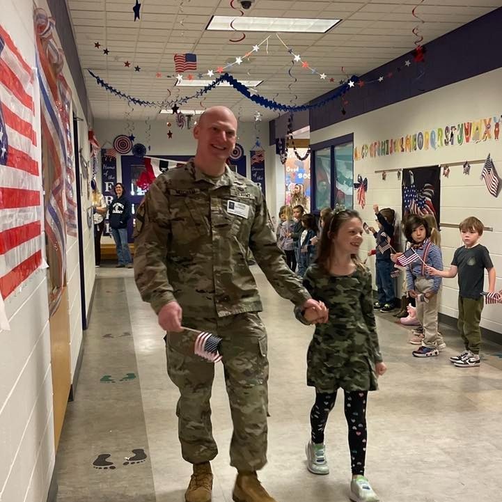 A military dad and his daughter walk down a school hallway during a Veteran's Day celebration.