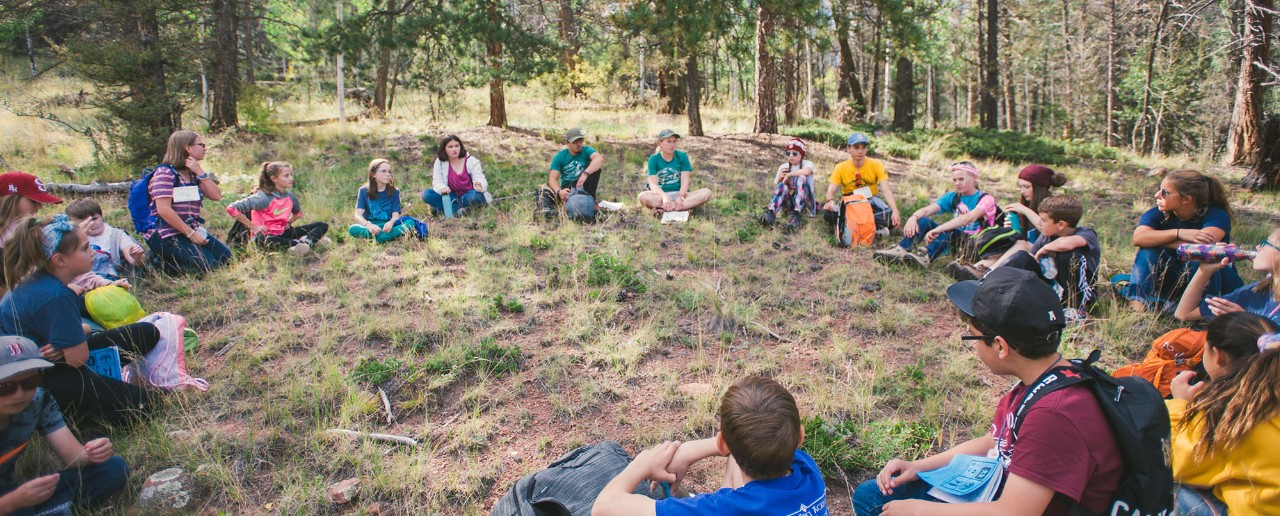 Students sit in a circle in the woods.