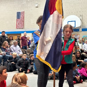 Two EES students place the CO flag in its stand during an assembly.