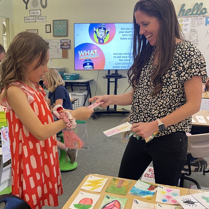 A teacher hands a student some fake money as part of a class project