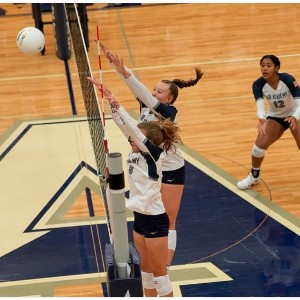 Two AAHS Volleyball players hit the ball across the net at a game.