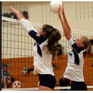 Two AAHS volleyball players jump to return the ball across the net.