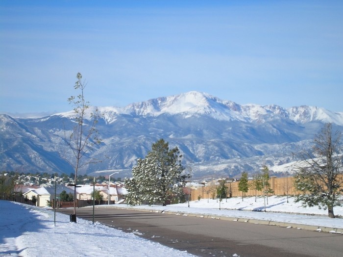 A neighborhood road gives way to a snow covered Pikes Peak in the background.